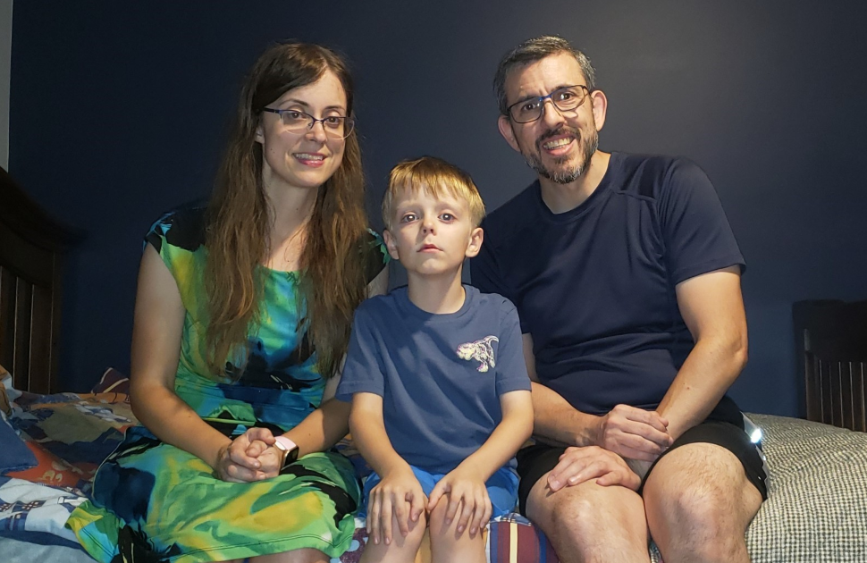 mom son and dad pose and smile while sitting on bed