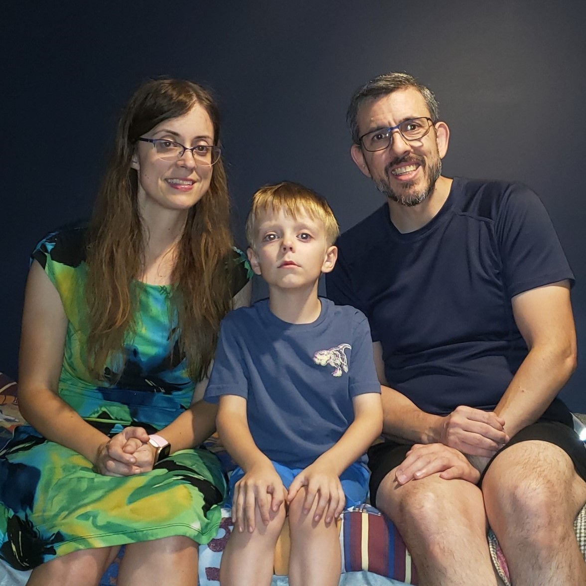 mom son and dad pose and smile while sitting on bed