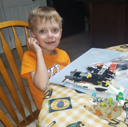 boy sits at table smiling and building lego