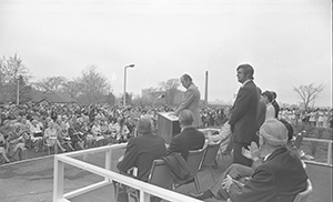 1974 greyscale image of people on a podium in front of a large crowd