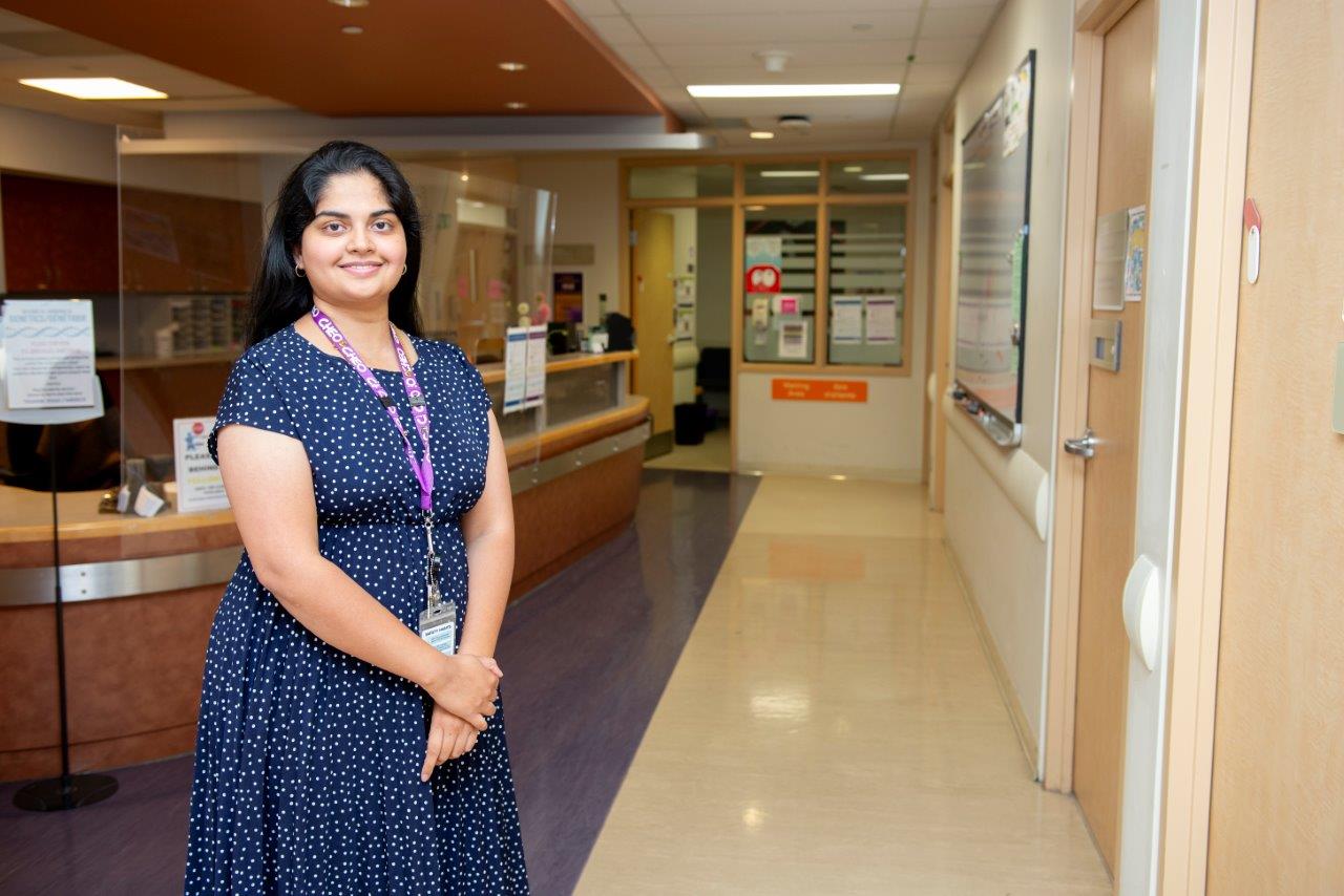 Divya wears a blue and white dress. She smiles and stands in front of reception.