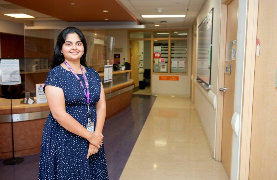 Divya wears a blue and white dress. She smiles and stands in front of reception.