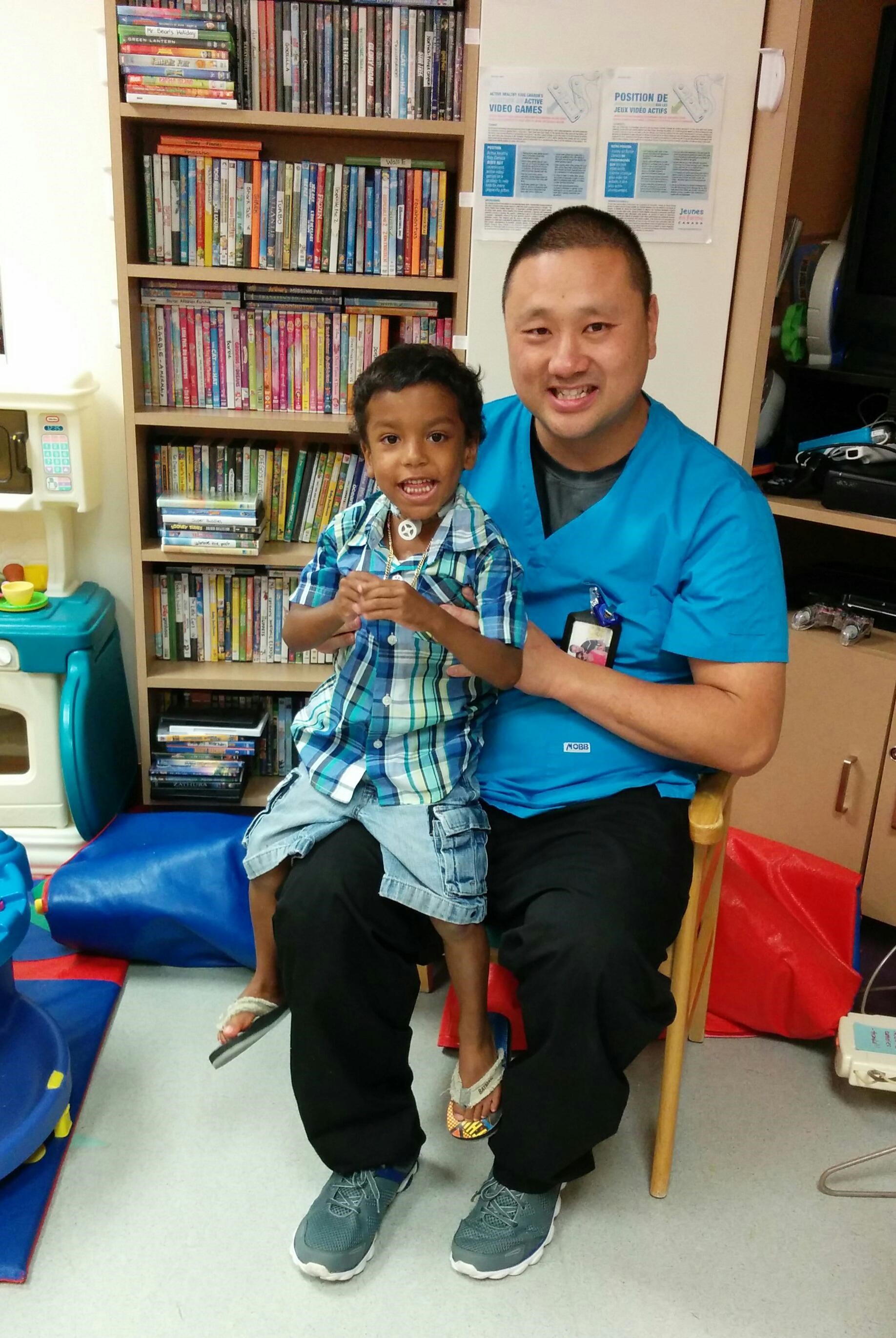 A man in grey scrubs with a little boy on his lap