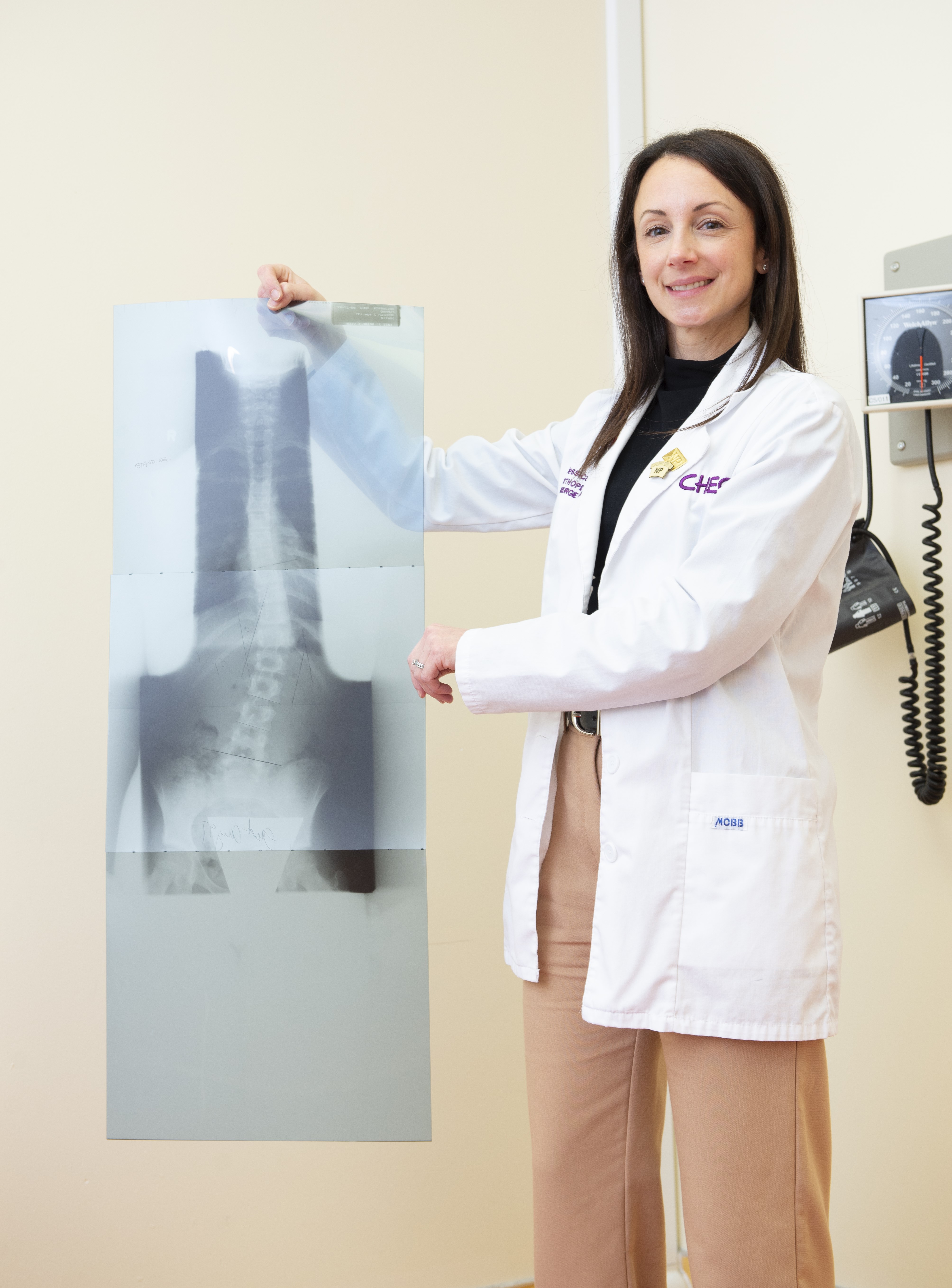 A woman with brown hair holds up an x-ray image of a spine