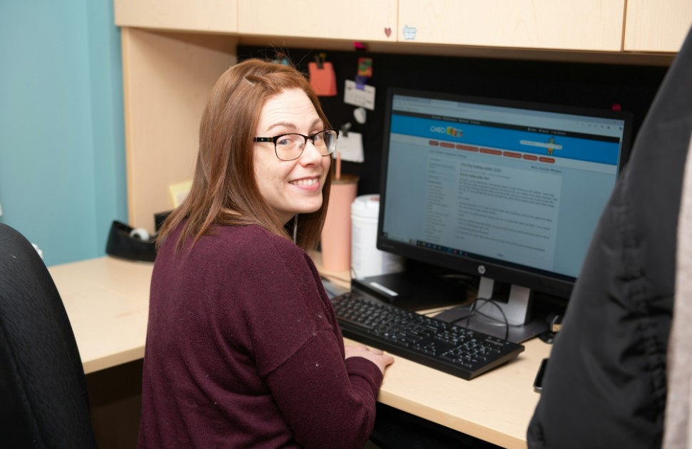 Lisa sits at her computer and smiles at the camera.