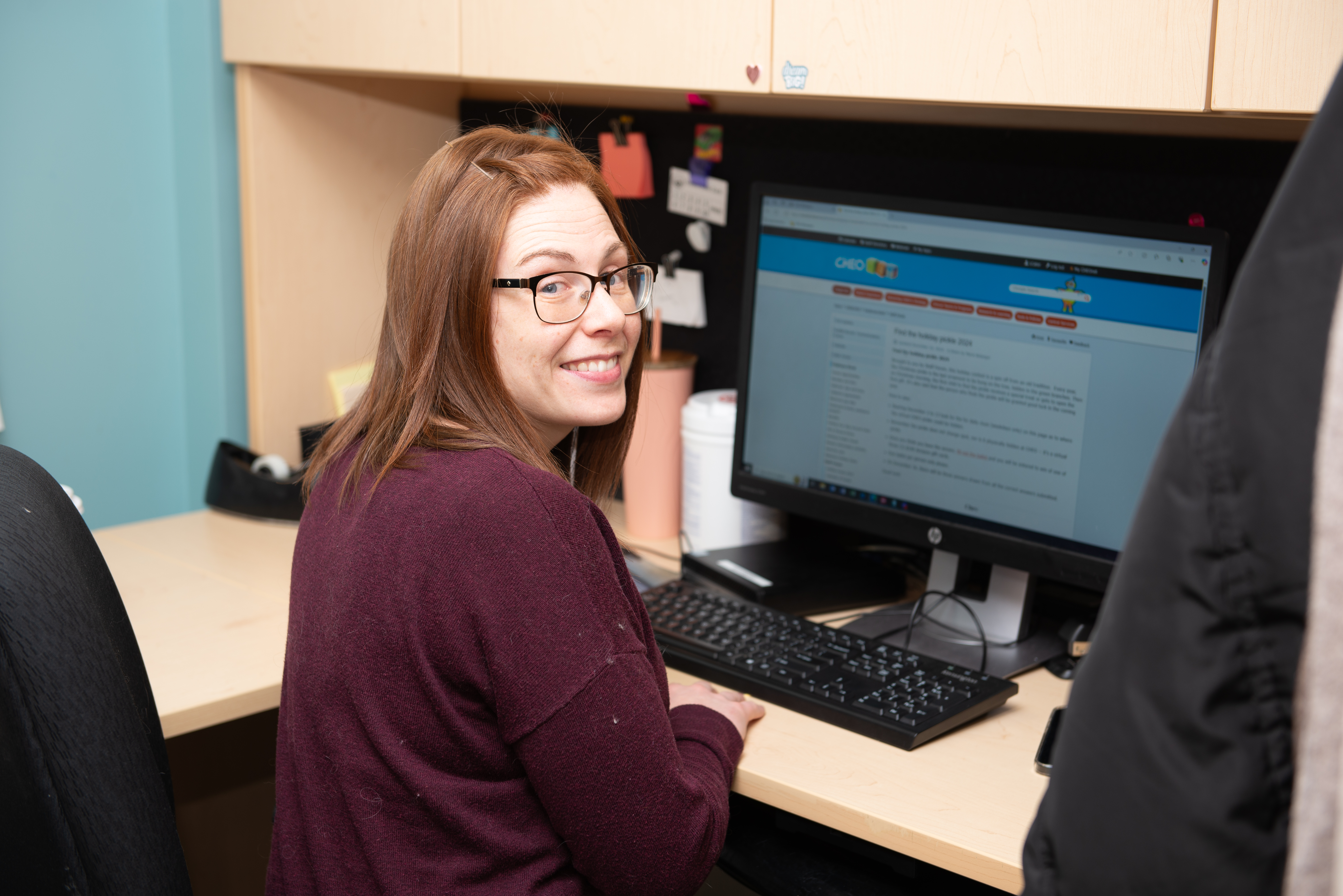 Lisa sits at her computer and smiles at the camera.