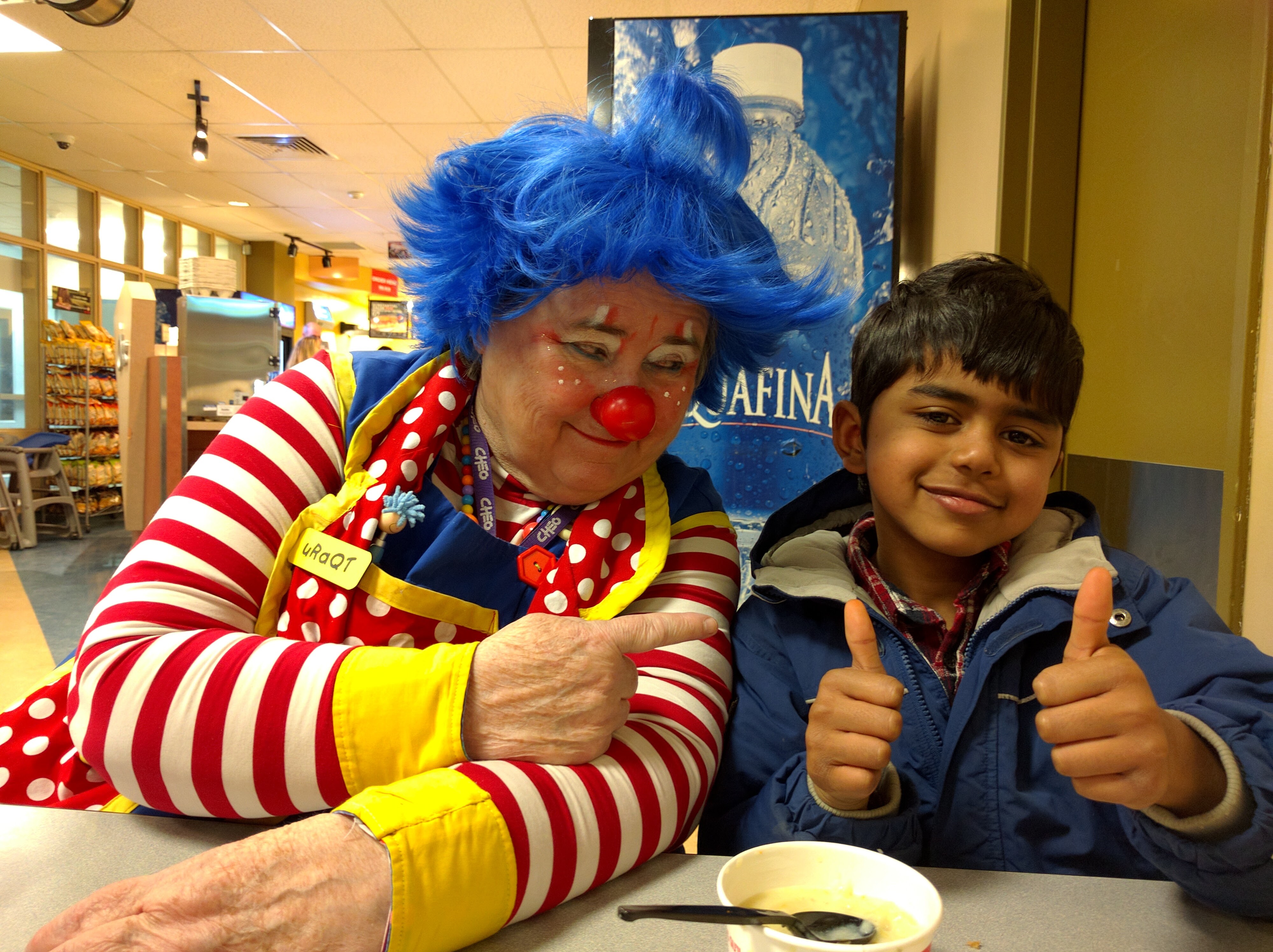 A young boy sitting with a clown at CHEO