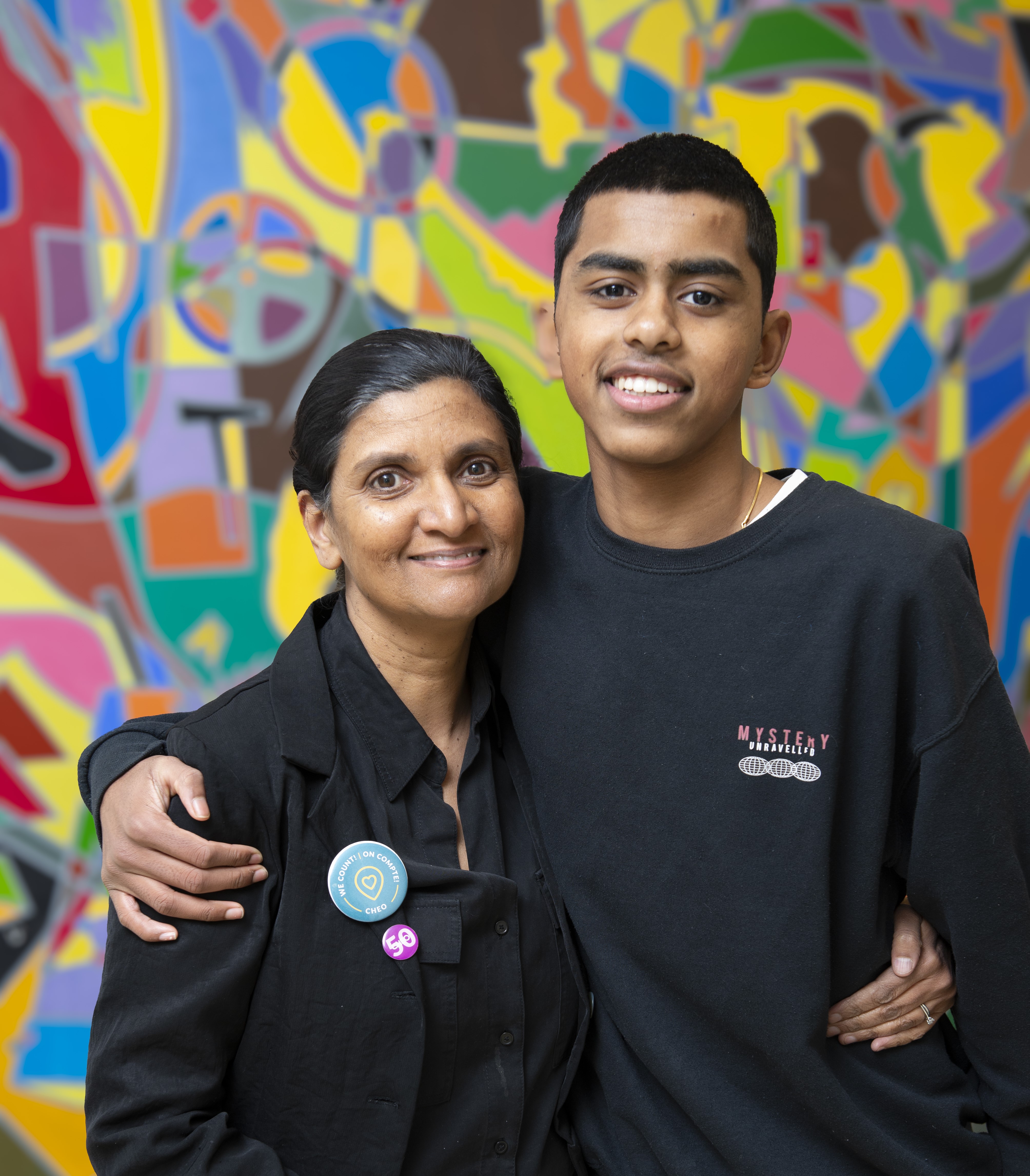 A woman standing next to her son in front of a colourful wall