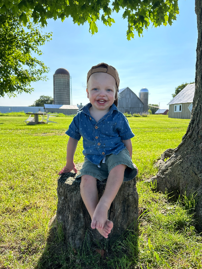 boy sits on tree stump smiling at camera