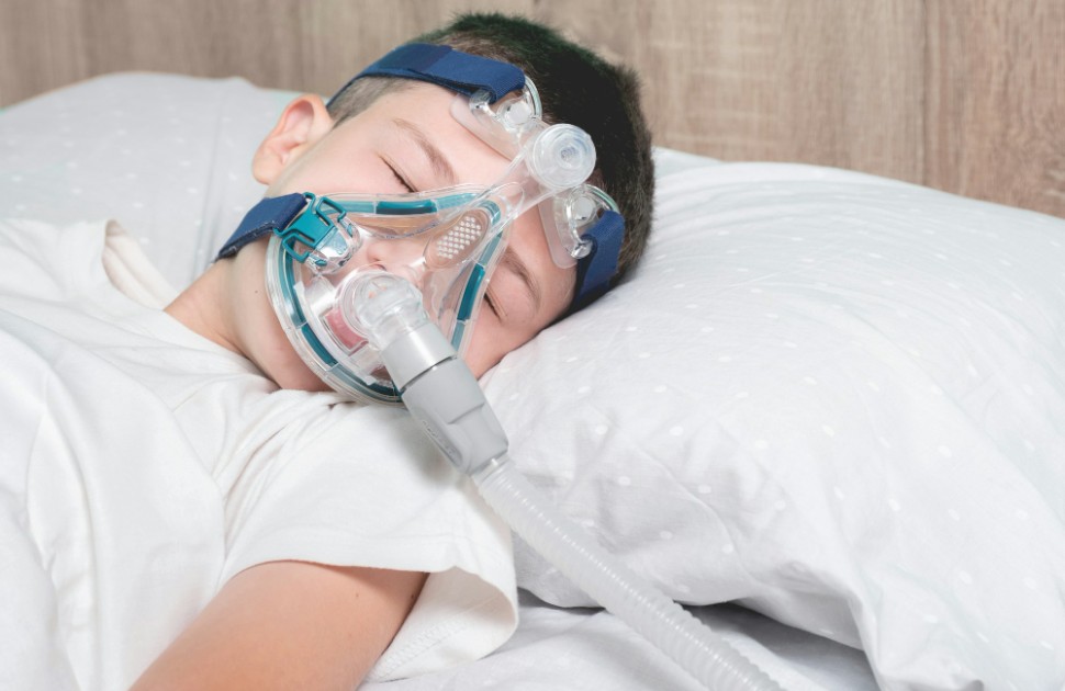 Child wearing a nebulizer mask on the hospital bed playing games in his smartphone
